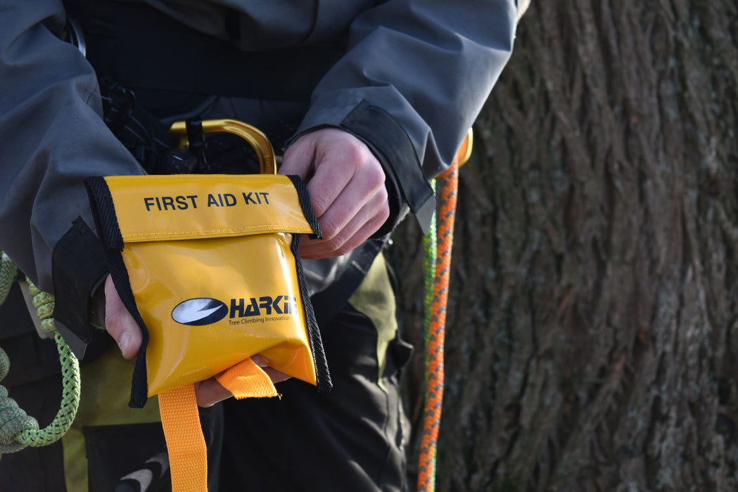 Harkie tree climbing first aid kit in yellow pouch held by arborist on harness beside climbing ropes